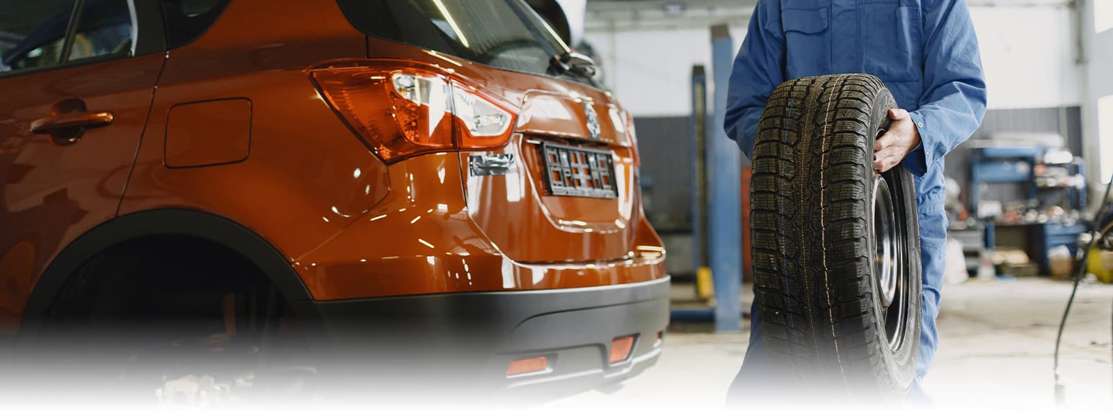 Photo of A Mechanic Behind The Orange SUV Holding A Spare Tire